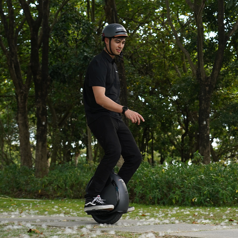 A man rides an INMOTION V6 electric unicycle in a park, wearing a helmet and casual outfit.
